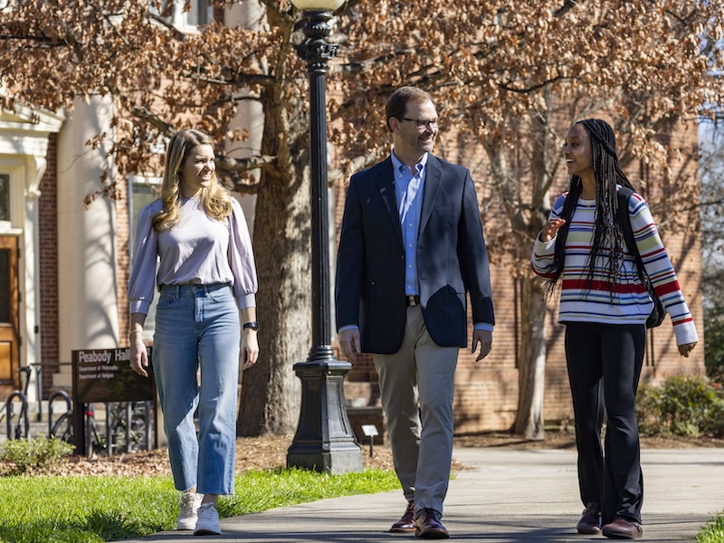 Derrick Lemons (center) walks with undergraduate students (L-R) Marguerite Epps and Gabriella Etienne near Peabody Hall.