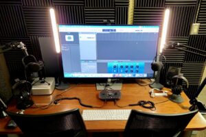 Image of a computer on a desk and podcasting equipment such as microphones, headphones, and speakers.